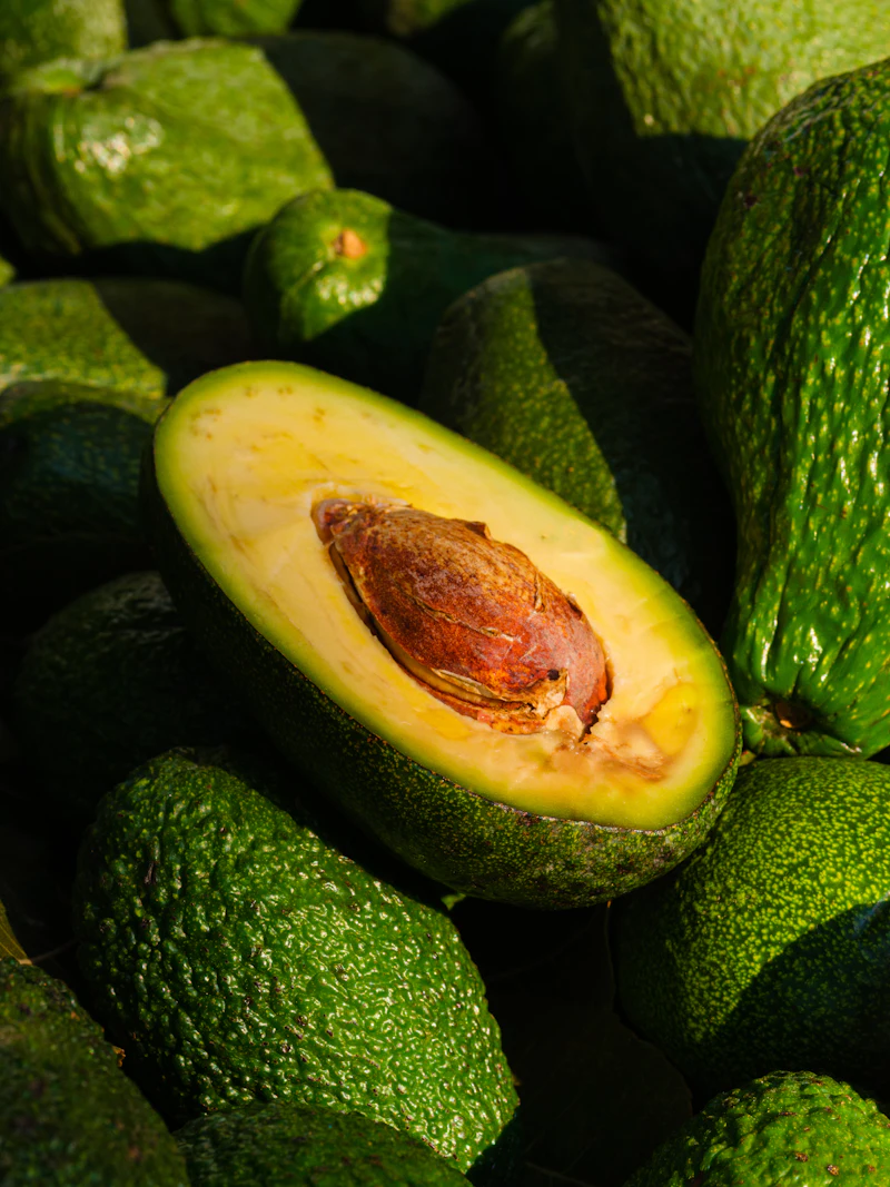 A halved avocado with its stone among whole fruit